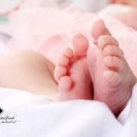 Tiny baby feet resting on a soft white blanket with a pink background