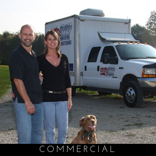 Two people and a dog posing beside a white commercial truck outdoors
