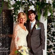 Bride and groom posing together at a wedding, with floral decorations in the background