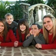 Five people in red sweaters leaning on a stone wall outdoors, smiling in a garden.