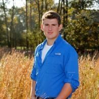 Man in a bright blue shirt standing in a field with trees in the background