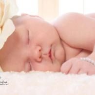 Sleeping baby resting on a white blanket with a soft pink background