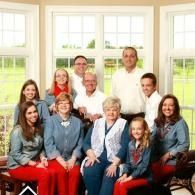 Group of eleven people posing indoors in front of bright windows, seated and standing in two rows.