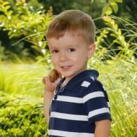 Smiling child in a navy striped shirt standing outdoors by green foliage