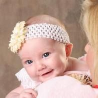 Smiling baby in white headband with cream flower, leaning on a pink cushion against a soft beige background