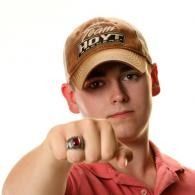 Young man in a tan cap points at the camera against a white background