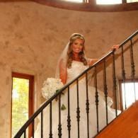 Bride in a white gown holding a bouquet on a curved staircase indoors