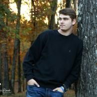 Person in a black sweater leaning against a tree in an autumn forest.