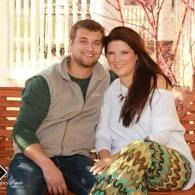 Two people sitting close together on a bench outdoors, smiling at the camera.