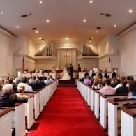 Wedding ceremony in a church aisle with guests seated on both sides of a red carpet