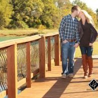 Couple standing on a wooden bridge, leaning close together in a sunny park.