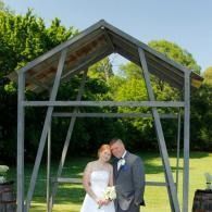 Bride and groom posing under a wooden arch in a garden setting