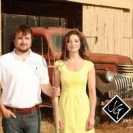 Two people standing in front of a red vintage truck and wooden barn, with a black-and-white logo in the corner.