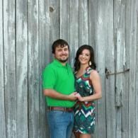 Smiling couple standing close together in front of a weathered wooden wall