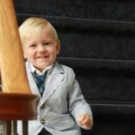 Smiling child in a light gray suit sitting on carpeted stairs