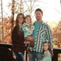 Family of four posing outdoors on a porch in fall, with autumn trees in the background.