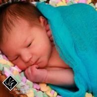 Sleeping newborn wrapped in a teal blanket on a colorful quilt