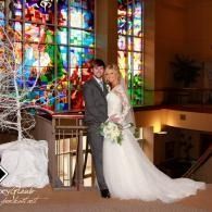Bride and groom posing in a church with colorful stained glass windows and floral decor