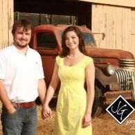 Two people holding hands in front of a rusted vintage truck and barn.