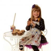 Girl sitting at a white table with snacks, holding a cookie and smiling