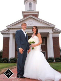 Bride and groom posing in front of a church, bride holding bouquet, groom in blue suit