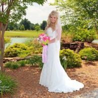 Woman in a white dress holding a pink bouquet in a garden by a pond