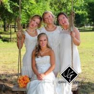 Four people in white dresses posing outdoors by a tree, with one seated and three standing behind her.