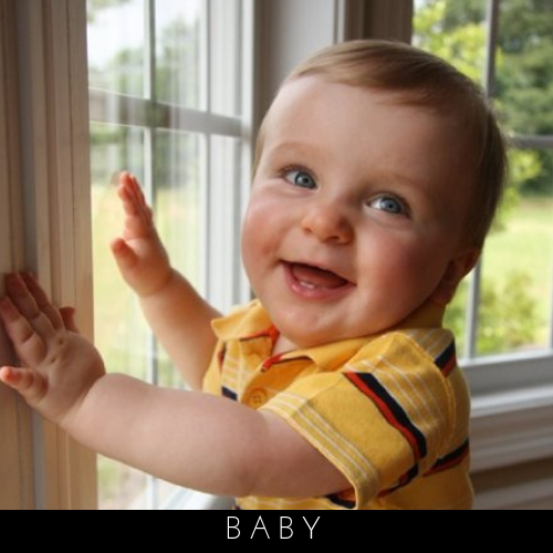 Smiling baby in a yellow shirt playing by a sunlit window
