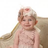 Smiling toddler in a pink dress and floral hat seated on a cream chair