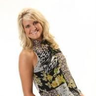 Blonde woman smiling in a black floral sleeveless top against a white background
