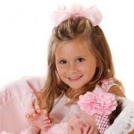 Smiling child in pink holding a little baby, with a fluffy pink bow and matching dress accents
