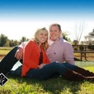 Couple sitting on grass in a sunny park, smiling with an arm around each other.