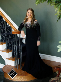 Woman in a black gown standing beside a staircase with white railing and wood steps