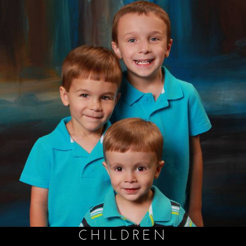 Three young children in turquoise shirts posing for a studio portrait, smiling at the camera.