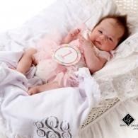 Baby in pink outfit lying on a white bed, with a pink 1 circle laying on top of her outfit and smiling.