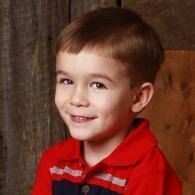 Young child in a red shirt smiling against a warm indoor backdrop