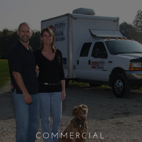 Two people and a dog standing beside a white commercial truck outdoors