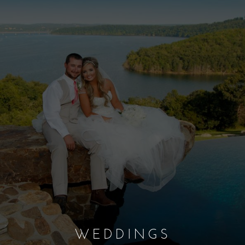 Wedding couple sitting by a pool with a lake and forested hills in the background