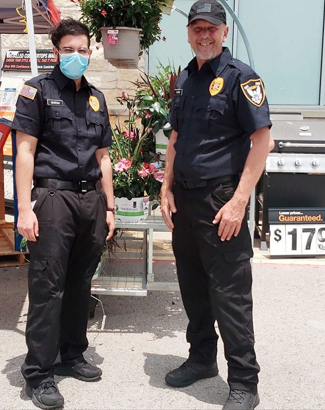 Two uniformed security officers standing beside a flower display and parked truck outdoors