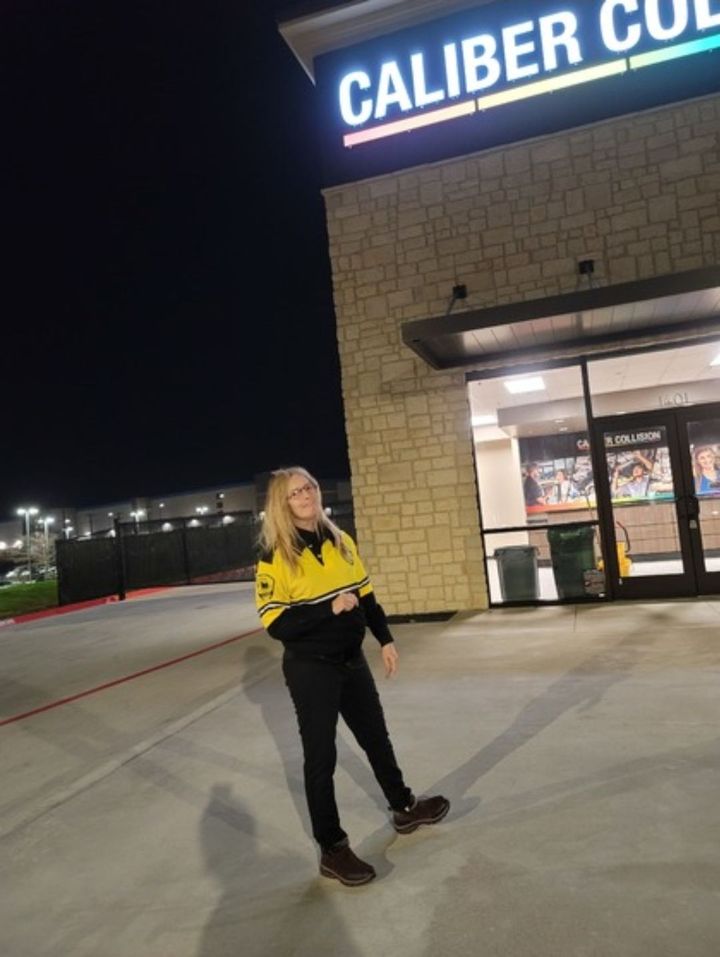 Person in a yellow jacket stands outside a Caliber Collision store at night.