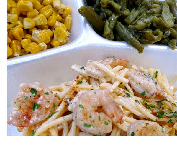 Tray with shrimp pasta, corn, and green beans in white compartments