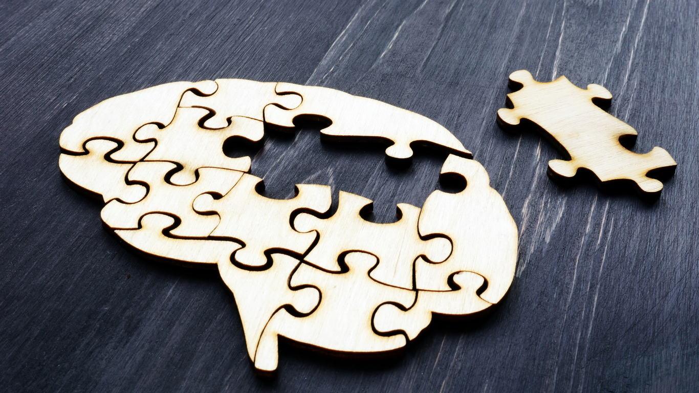 White puzzle-shaped brain with a missing piece and one loose puzzle piece on a dark surface