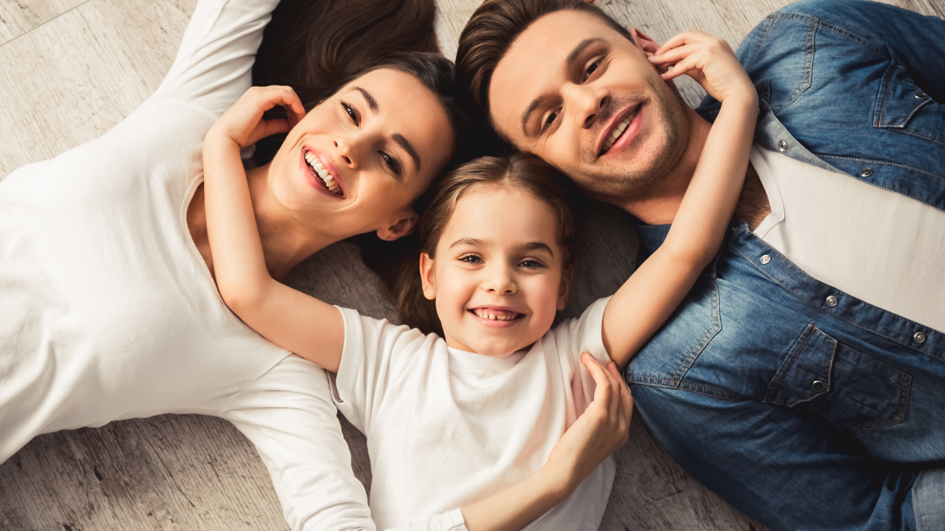 Family of three lying on a bed, smiling and embracing each other.