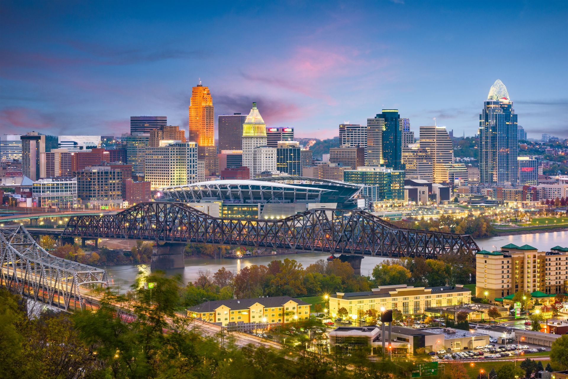Downtown Cincinnati skyline at dusk with lit bridge spanning the river