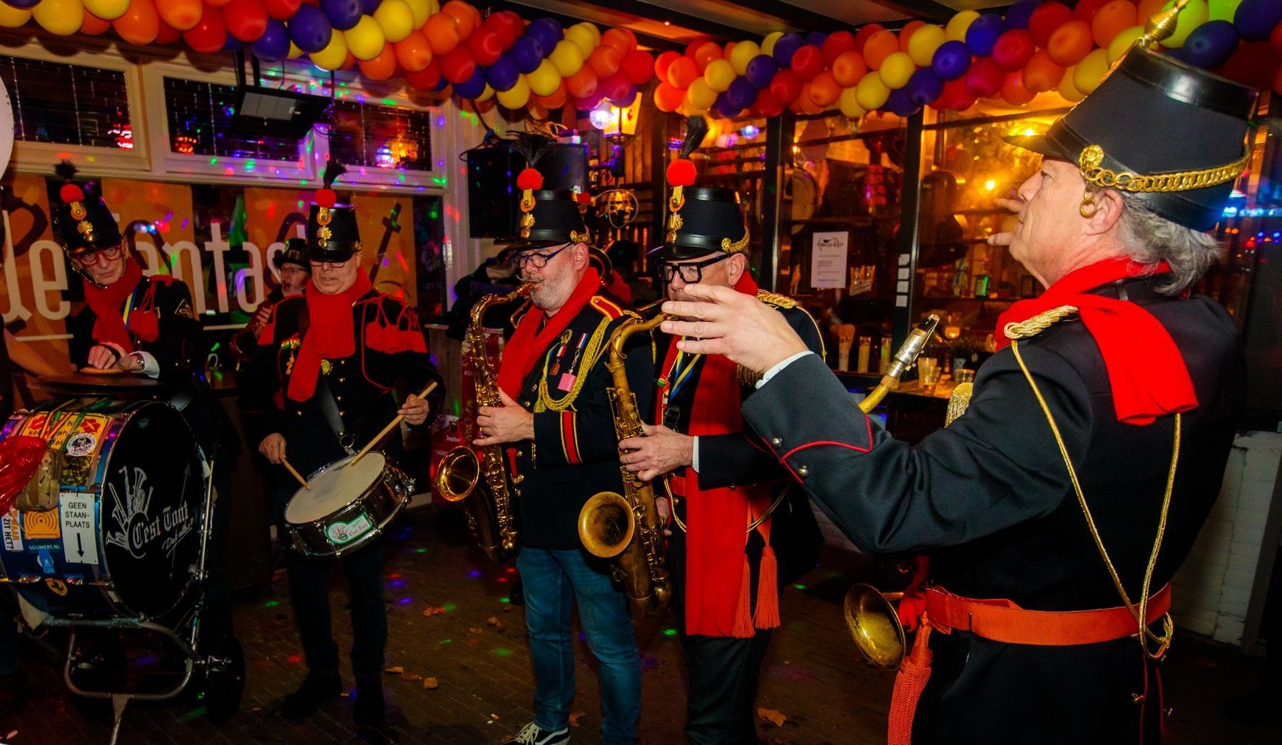 Een groep mannen bespeelt een instrument in een kamer met ballonnen.