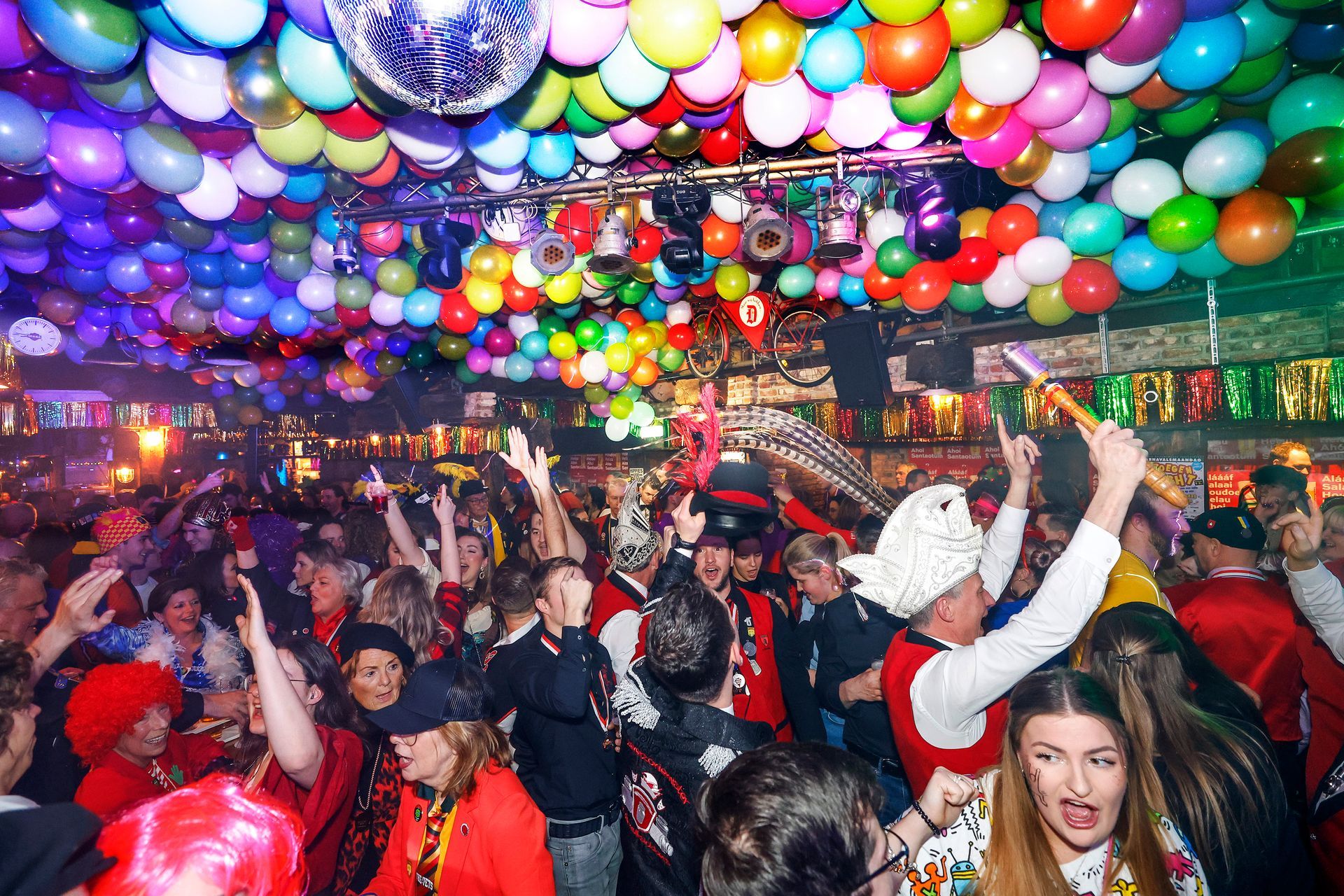 Een groep mensen danst in een club met ballonnen die aan het plafond hangen.