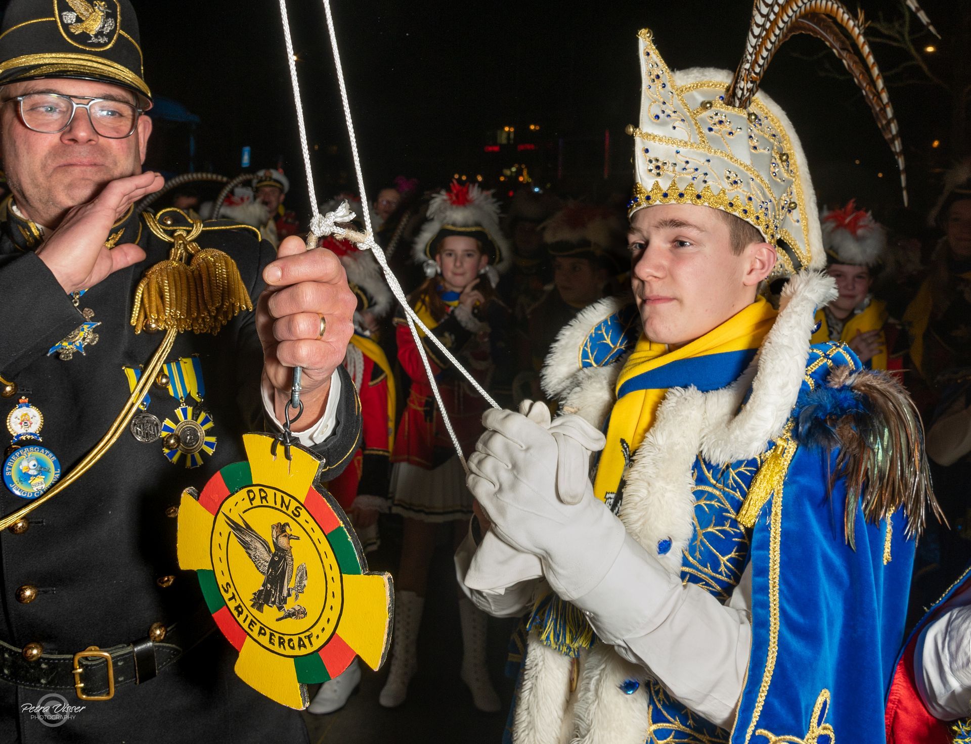 Een man in militair uniform houdt een touw vast naast een jongen in een carnavalskostuum
