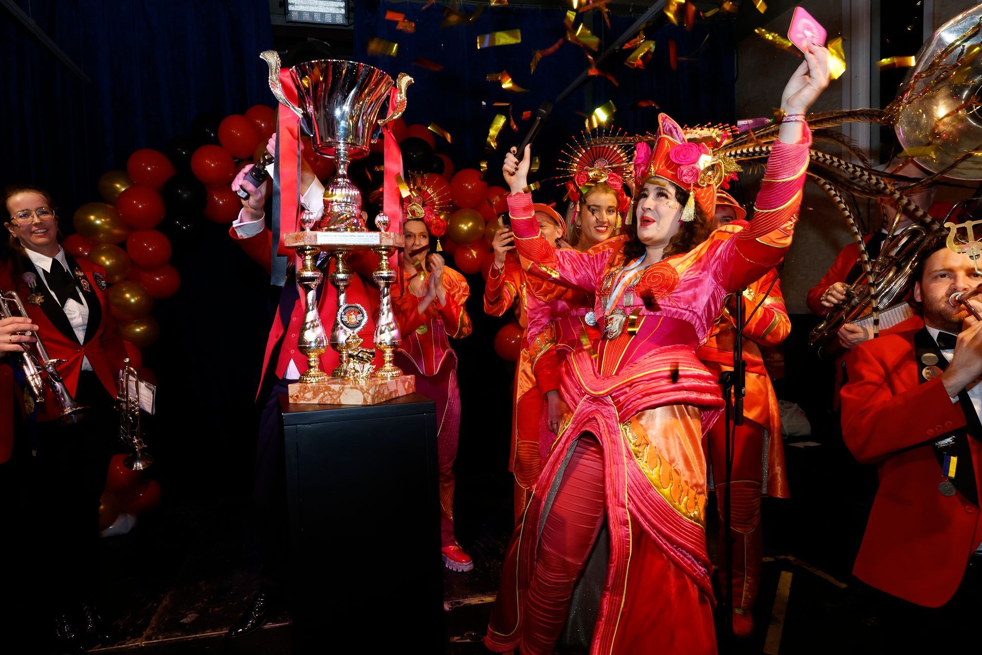 Een groep mensen in rode kostuums staat rond een trofee.