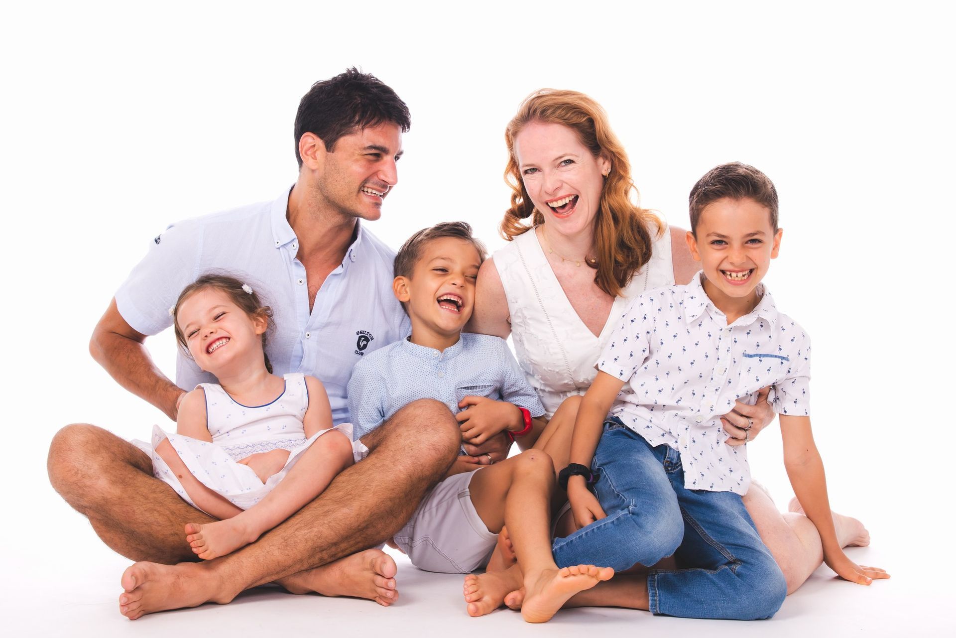 Family of five sitting and laughing together, against a white background.