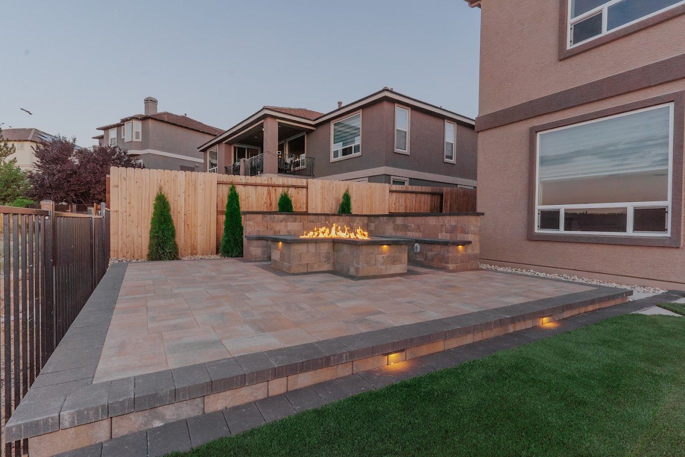 Backyard patio with stone seating wall, built-in fire pit, and wood fence beside a house